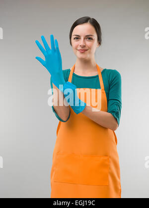 Felice giovane donna di pulizia di mettere dei guanti di gomma Foto Stock
