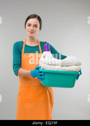 Giovane donna tenendo gli asciugamani puliti e detersivo in vasca contro uno sfondo grigio. studio fotografico Foto Stock