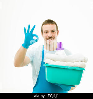 Ritratto di uomo caucasico cestello di contenimento con lavanderia, sorridente e mostra ok segno, su sfondo bianco Foto Stock