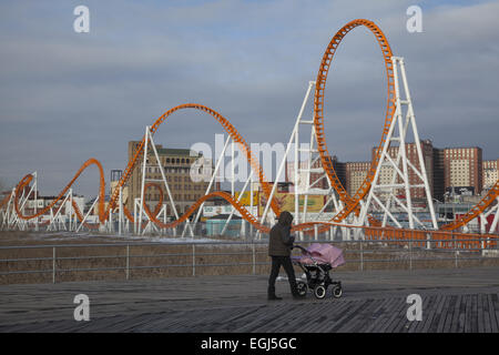 La donna spinge un gemelli passeggino bimbo lungo la passeggiata a mare di Coney Island con il Thunderbolt Roller Coaster in background dur Foto Stock