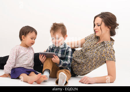 Giovane madre con due bambini guardare cartoni sul cellulare su sfondo bianco Foto Stock