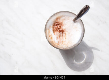 Cappuccino schiumoso in un caffè di vetro con cucchiaio su marmo bianco superficie all'aperto dall'alto. Foto Stock