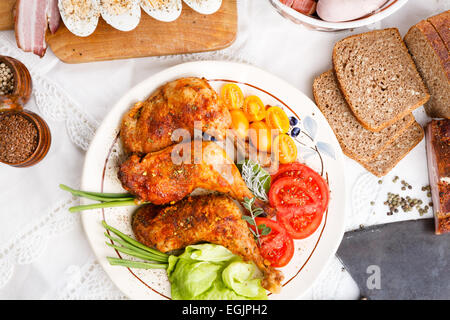 Arrosto di tacchino gambe wit insalata di pomodori erbe sulla tovaglia bianca, vista dall'alto Foto Stock