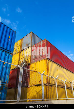 Colorate cargo industriale contenitori vengono impilati sotto blu cielo nuvoloso dietro la recinzione metallica con filo spinato. Foto verticale Foto Stock