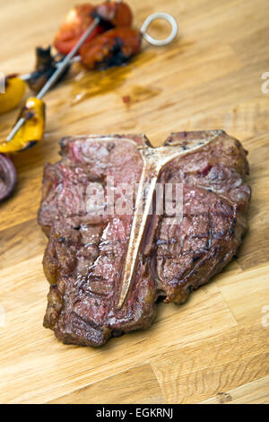 T-bone steak su pannello di legno con i germogli vegetali in background Foto Stock