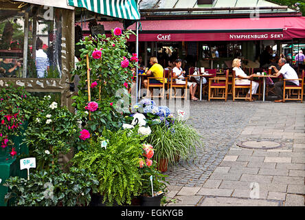 Un caffè all'aperto vicino a fiori offerte di stallo libero per gli acquirenti del Viktualienmarkt, famoso mercato nel centro di Monaco di Baviera Foto Stock