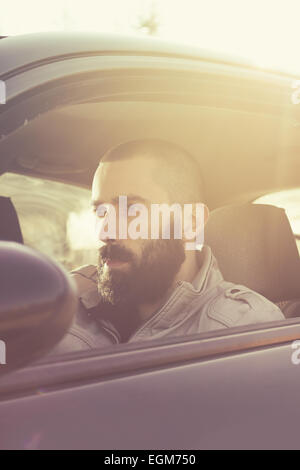 Giovane uomo bello alla guida della sua auto in una bella giornata di sole. Toni rétro. Foto Stock