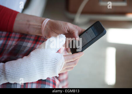 Masterizzazione femmina paziente con mano bendato e braccio utilizzando Smart Phone Foto Stock