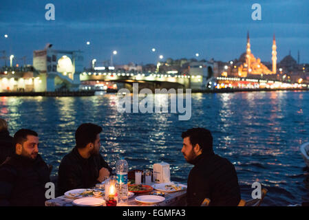 ISTANBUL, Turchia / Türkiye - i commensali mangiano in ristoranti all'aperto sulle rive del Corno d'Oro a Karakoy, con il ponte Galata e la nuova moschea sullo sfondo. Foto Stock