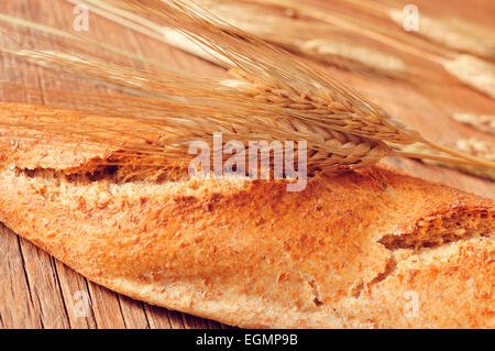 Primo piano di un grano intero baguette e alcune spighe di grano su una tavola in legno rustico Foto Stock