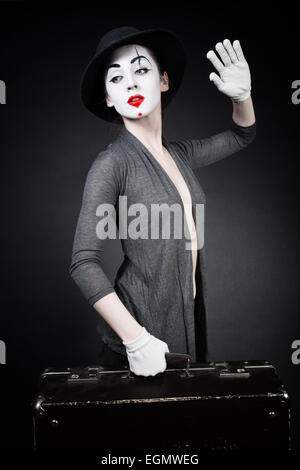 Donna mime in hat con la valigia su sfondo nero Foto Stock