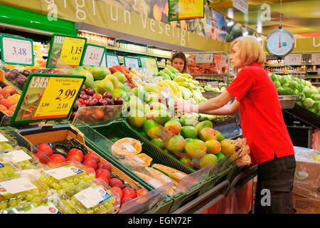 Riga, Lettonia. Interno del ipermercato Rimi lettone store. Assistente di ripiani di impilamento al di frutta fresca e vegetali di stallo del contatore Foto Stock