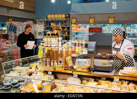 Riga, Lettonia. Interno del ipermercato Rimi lettone store. Assistente e il cliente al caseificio contatore deli con shopping list Foto Stock