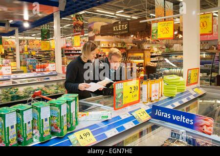 Riga, Lettonia. Interno del ipermercato Rimi lettone store. I clienti giovane a cibi congelati a base di pesce contatore deli con shopping list Foto Stock