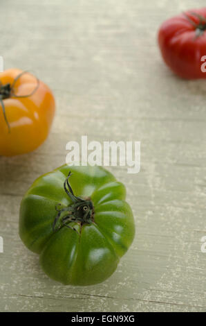 Verde, giallo e rosso dei pomodori cimelio disposti su un rustico di legno verde pallido sfondo. Foto Stock