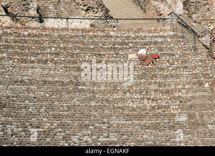 Una donna cercando di leggere, rivolta lontano dal sole luminoso mentre seduto presso le rovine romane a Lione, Francia Foto Stock