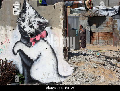 (150227) -- GAZA, 27 febbraio 2015 (Xinhua) -- Una donna Palestinese sorge accanto a un murale di un gattino che è stato dipinto da British artista di strada Banksy sui resti di un tempio che fu distrutto durante la 50-giorno offensiva israeliana sulla Striscia di Gaza negli ultimi mesi di luglio e agosto, nel nord della Striscia di Gaza città di Beit Hanun nel febbraio 27, 2015 (Xinhua/Yasser Qudih) Foto Stock