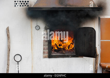 Forno in pietra con il fuoco dentro le fiamme e il fumo nero proveniente dalla porta. Foto Stock