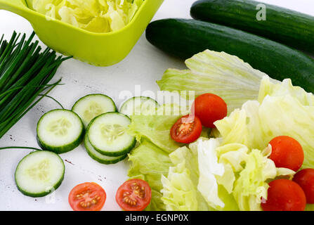 Preparazione di insalate con cetrioli, lattuga, pomodori ciliegini e erba cipollina sul moderno in legno bianco impostazione tabella, primo piano. Foto Stock