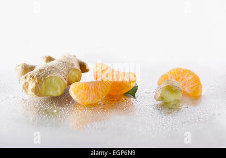 Lo zenzero Zingiber officinale root con Mandarin, Citrus reticulata, pezzi disposti su sfondo argento e spritzed con acqua. Messa a fuoco selettiva. Foto Stock