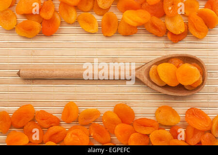 Il cucchiaio di legno con albicocche secche giacente sul tappetino di bambù Foto Stock