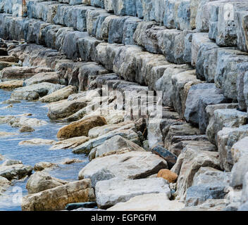 La curvatura breakwall di pietre impilate sull'acqua. Foto Stock