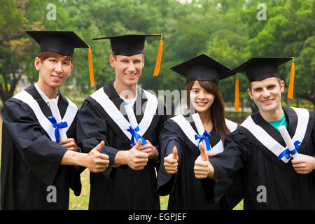 Felice gli studenti di laurea gli abiti che mostra diplomi con il pollice in alto Foto Stock