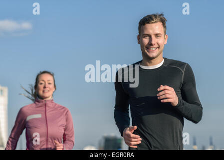 Basso angolo superiore vista del corpo contro il cielo blu e chiaro di un sorridente uomo bello fare jogging con sua moglie in una salute e concetto di fitness Foto Stock