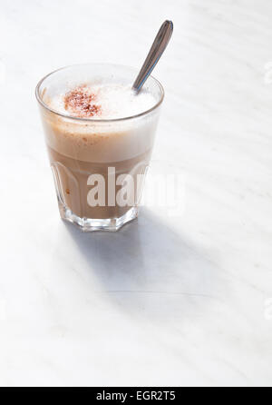 Cappuccino schiumoso in un caffè di vetro con cucchiaio su marmo bianco tavola dal lato. Foto Stock