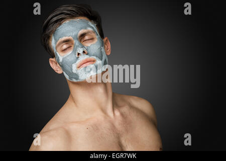 Ritratto di un bel giovane con un viso maschera di argilla, cura del viso e del corpo il trattamento. Foto Stock