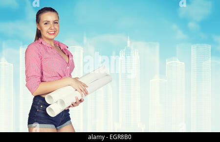 Donna in jeans brevi holding di rotoli di carta, sorridente. Filo-frame di edifici come sfondo Foto Stock