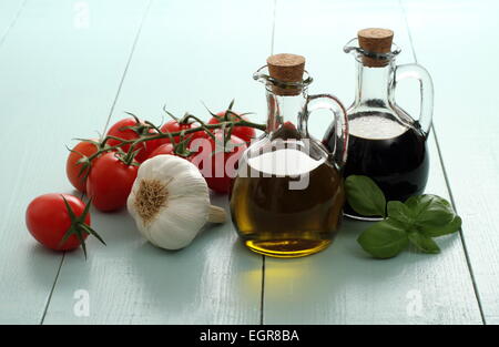 Olio di oliva e aceto in vendemmia bottiglie sul tavolo di legno, pomodorini con aglio Foto Stock