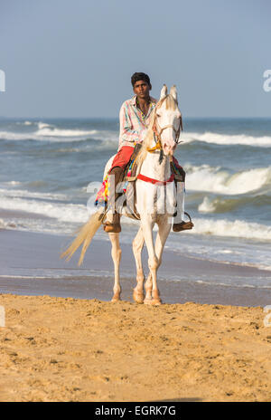 Uomo locale in sella ad un cavallo bianco in riva al mare sulla spiaggia di Marina, Chennai, nello Stato del Tamil Nadu, nell India meridionale Foto Stock