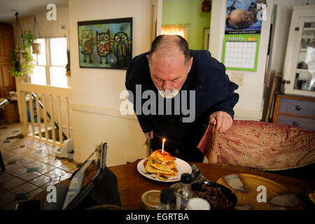 L uomo nella sua 50s soffiando fuori le candele sulle frittelle di compleanno per il suo compleanno Foto Stock