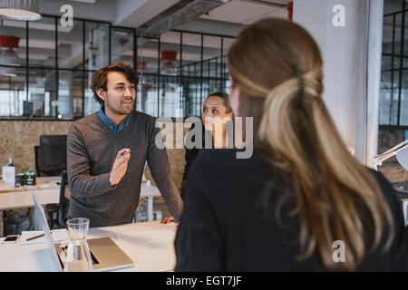 Giovane uomo che illustra il nuovo business plan ai colleghi di lavoro durante un incontro intorno a un tavolo in ufficio. Foto Stock