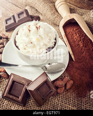 Tazza di cioccolata calda con panna montata, cacao in polvere, le fave di cacao e pezzi di cioccolato. Foto Stock