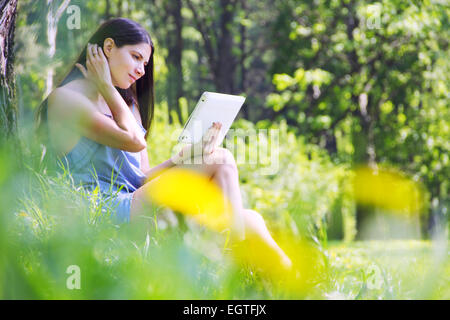 Giovane donna con tavoletta di seduta per esterno erba verde con fiori Foto Stock