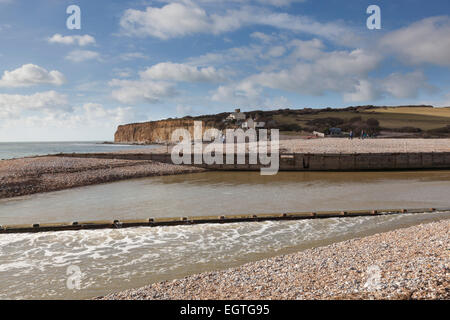 L'estuario del fiume Cuckmere che fluisce nel mare ad alta marea con il vecchio coastguard cottages sulla scogliera dietro. Foto Stock