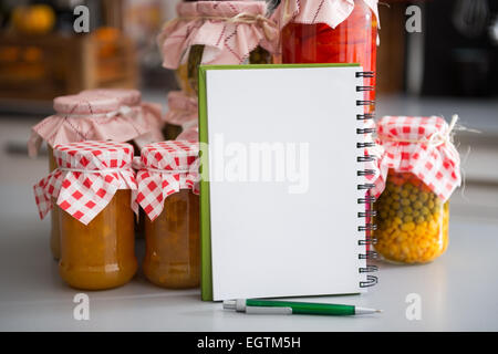 Primo piano su notepad tra giare con fatti in casa marmellata di frutti e verdure sottaceto Foto Stock