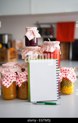 Primo piano su notepad tra giare con fatti in casa marmellata di frutti e verdure sottaceto Foto Stock