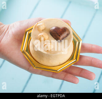 Piccola torta di nocciole e cioccolato fondente al cuore in mano femminile. Foto Stock