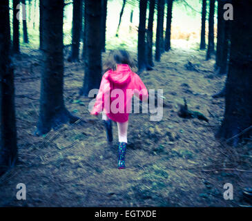 Giovane ragazza in cappotto rosa acceso verso la luce al di fuori della foresta. Foto Stock
