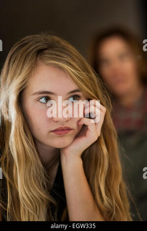 Teen figlia in appoggio il suo mento nella sua mano, Madre in background. Foto Stock