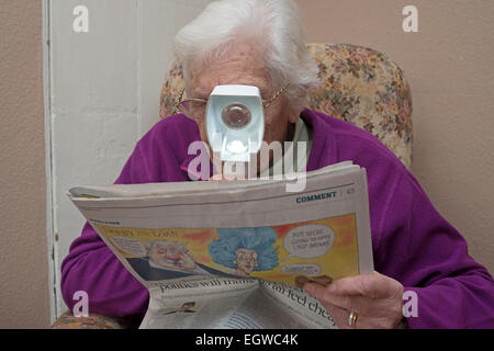 Donna affetti da degenerazione maculare senile usando un'illuminata lente di ingrandimento per leggere un giornale Foto Stock