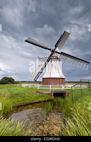 Il mulino a vento di bianco dal fiume di oltre il cielo velato, Olanda Foto Stock