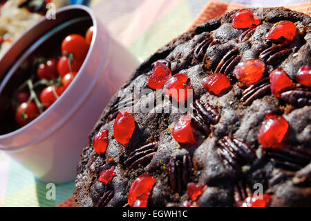 Cioccolato Torta di noci e rabboccato con ciliegie, accanto a una pentola di pomodori ciliegia. Foto Stock