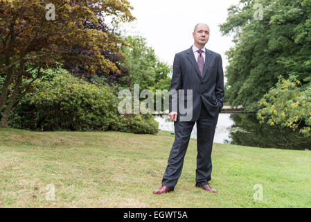 Un imprenditore professionale / hotel manager sta nei giardini di una casa di campagna inglese che indossa una tuta di business Foto Stock