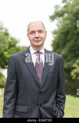 Un imprenditore professionale / hotel manager sta nei giardini di una casa di campagna inglese che indossa una tuta di business Foto Stock