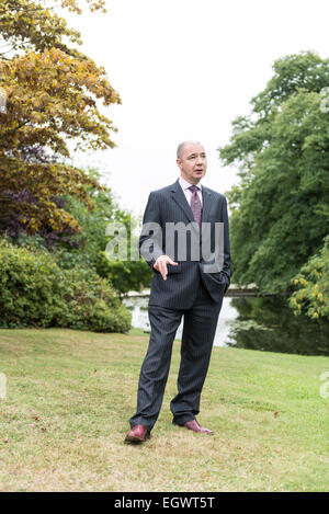 Un imprenditore professionale / hotel manager sta nei giardini di una casa di campagna inglese che indossa una tuta di business Foto Stock