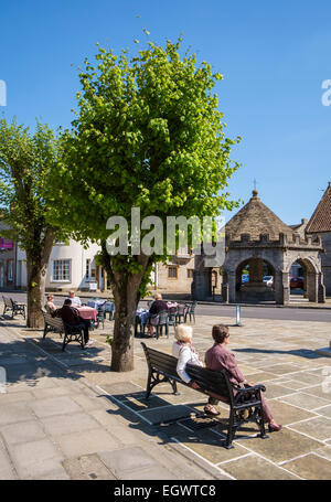 Somerton, una bella piccola vecchia città mercato nel Somerset, Inghilterra, Regno Unito con croce di mercato e la gente seduta su una panchina Foto Stock